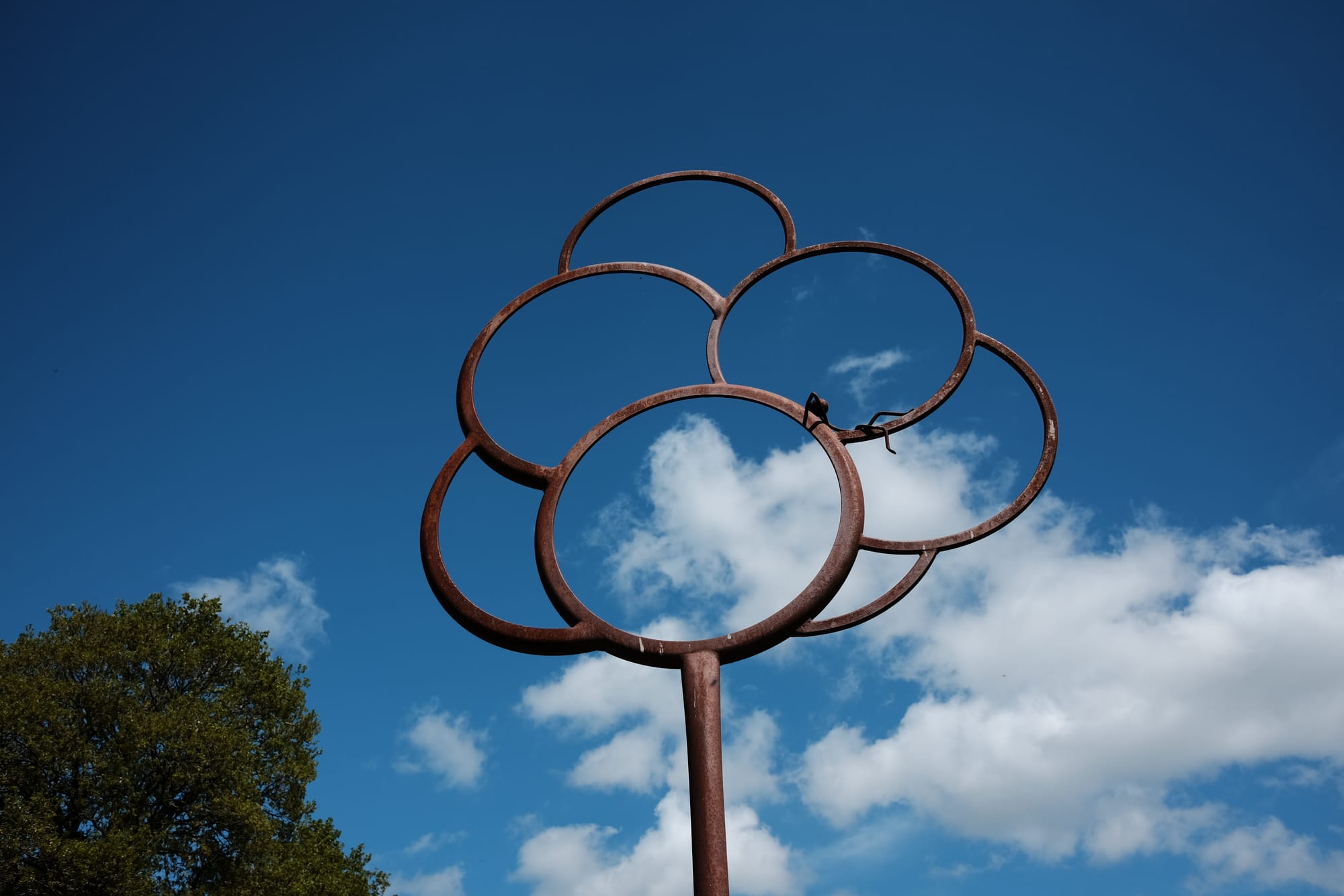 A rusty brown geometric sculpture comprised of interlocking circles – a human figure laying in one of them – is pictured against a blue sky