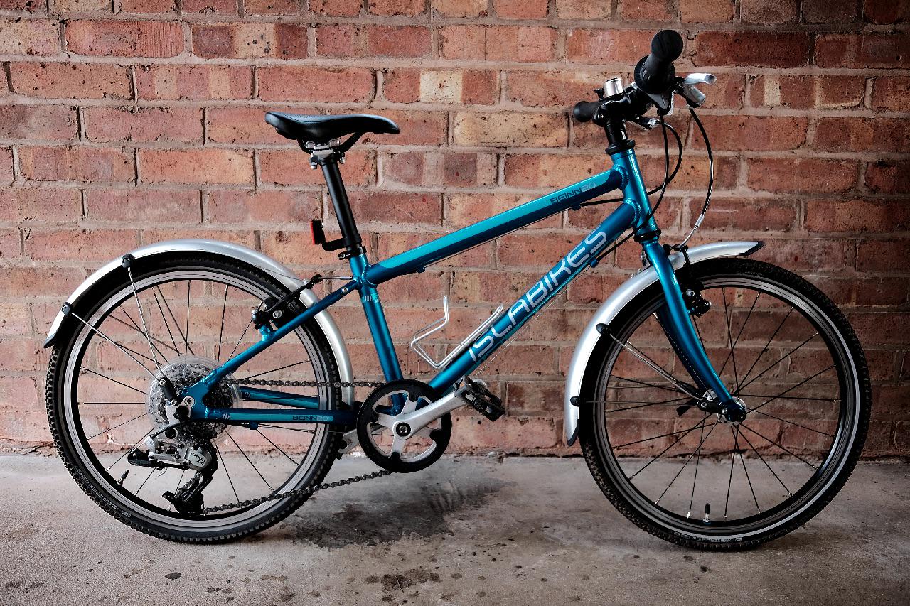 A turquoise child's 20" Islabike leans against a brick wall.