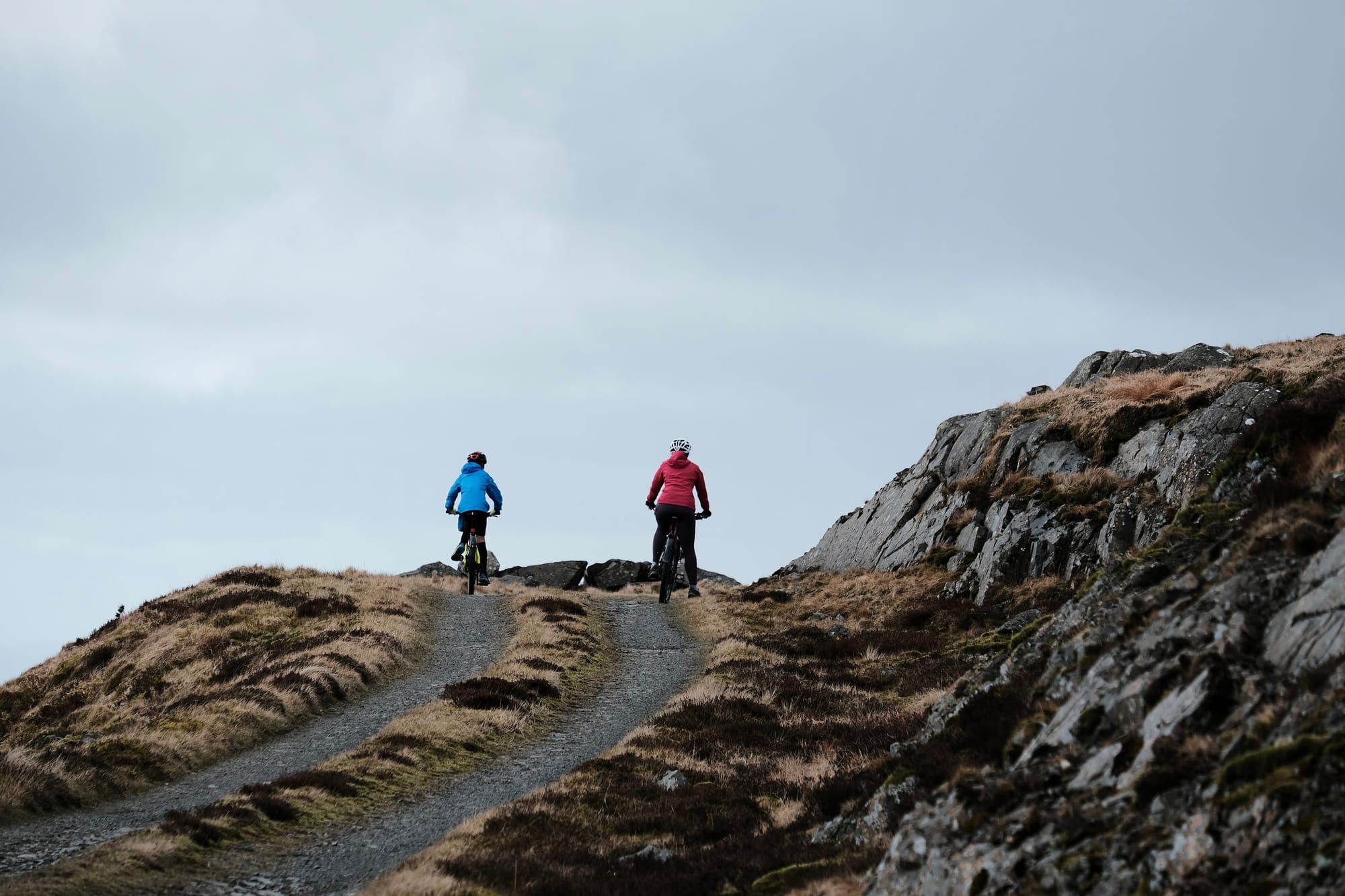 Two cyclists – one dressed in blue and the other in pink – pause at the top of a steep rocky track.