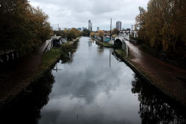 A black canal viewed from a bridge, with the towers of a city in the distance.